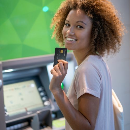 Portrait of a happy woman making a cash withdrawal on an ATM and looking at the camera smiling